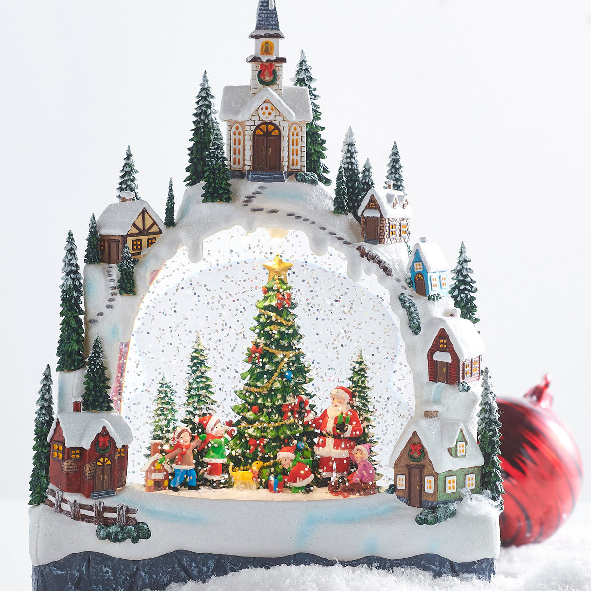 Decorative Christmas scene water lantern with a church, trees, and Santa Claus figures on a snowy base.