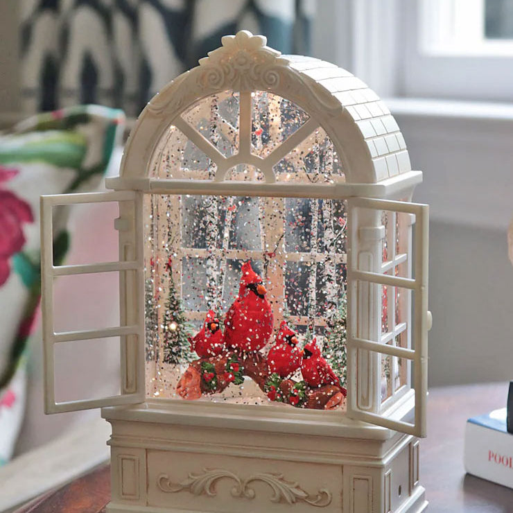 Decorative snow globe with a cardinal and red berries on a wooden surface.