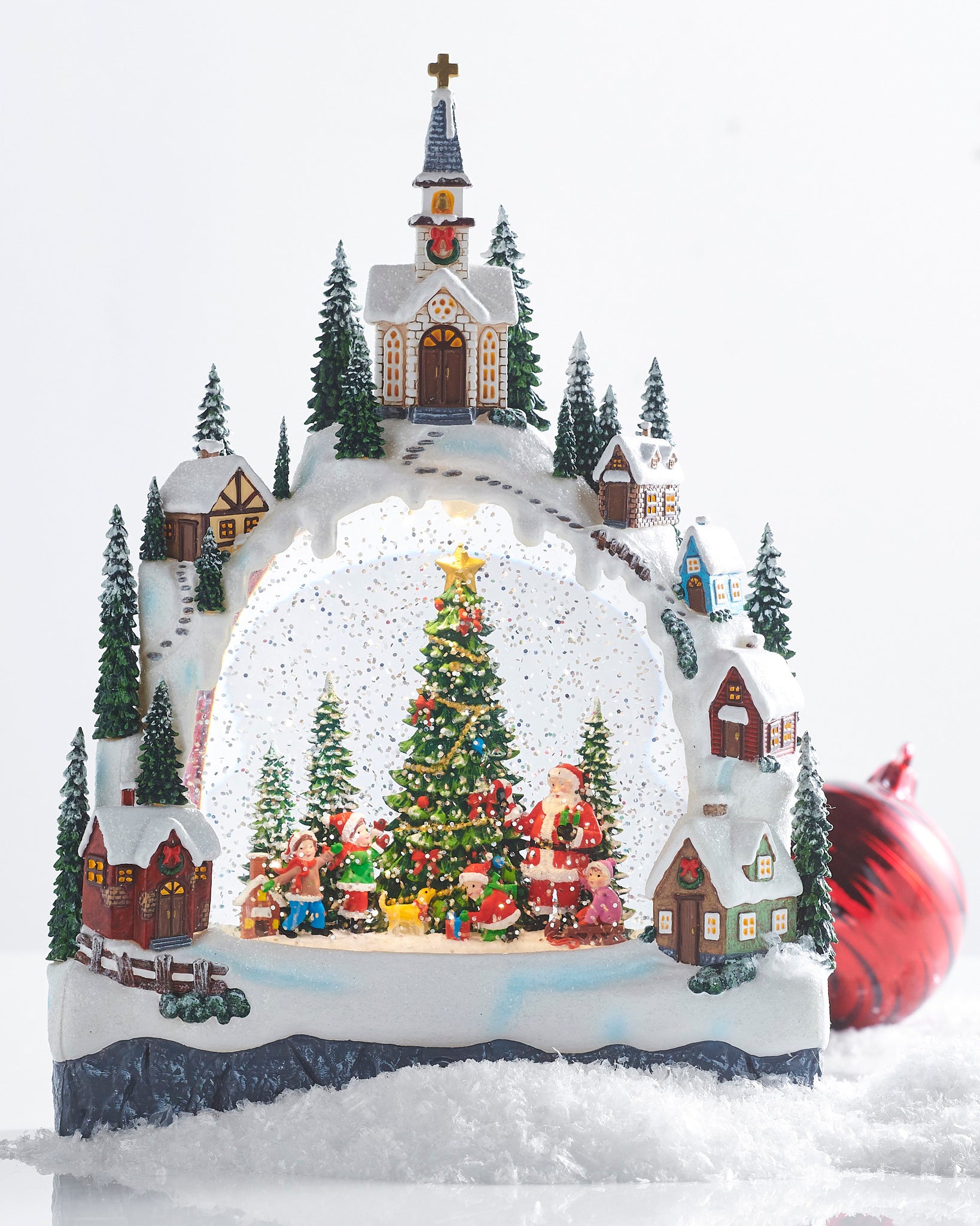 Decorative Christmas scene water lantern with a church, trees, and Santa Claus figures on a snowy base.