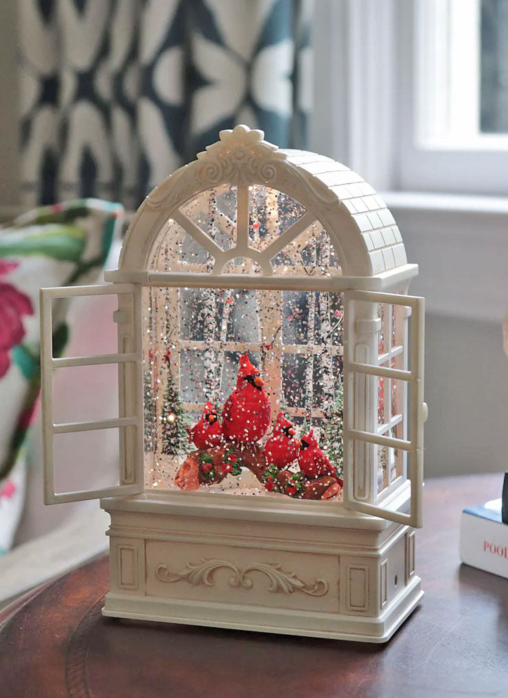 Decorative snow globe with a cardinal and red berries on a wooden surface.
