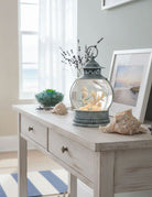 Decorative table with a snow globe, shells, and a framed picture in a room with a window.